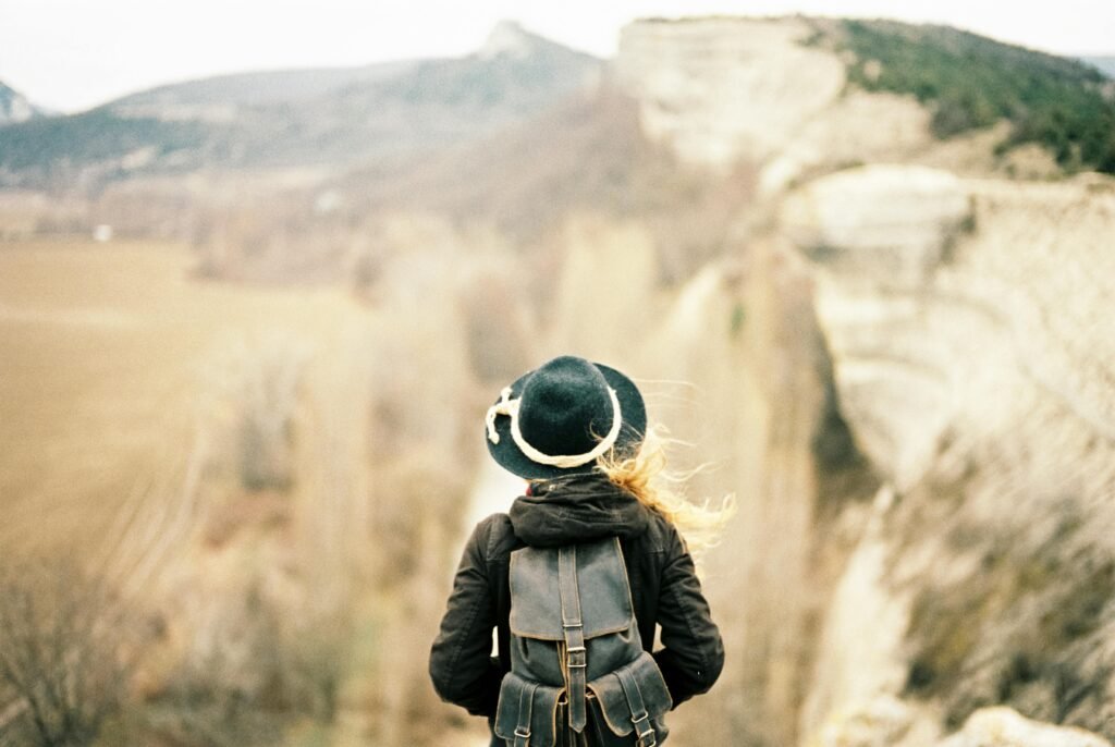 A woman with a backpack admires a stunning mountain view, symbolizing adventure.
